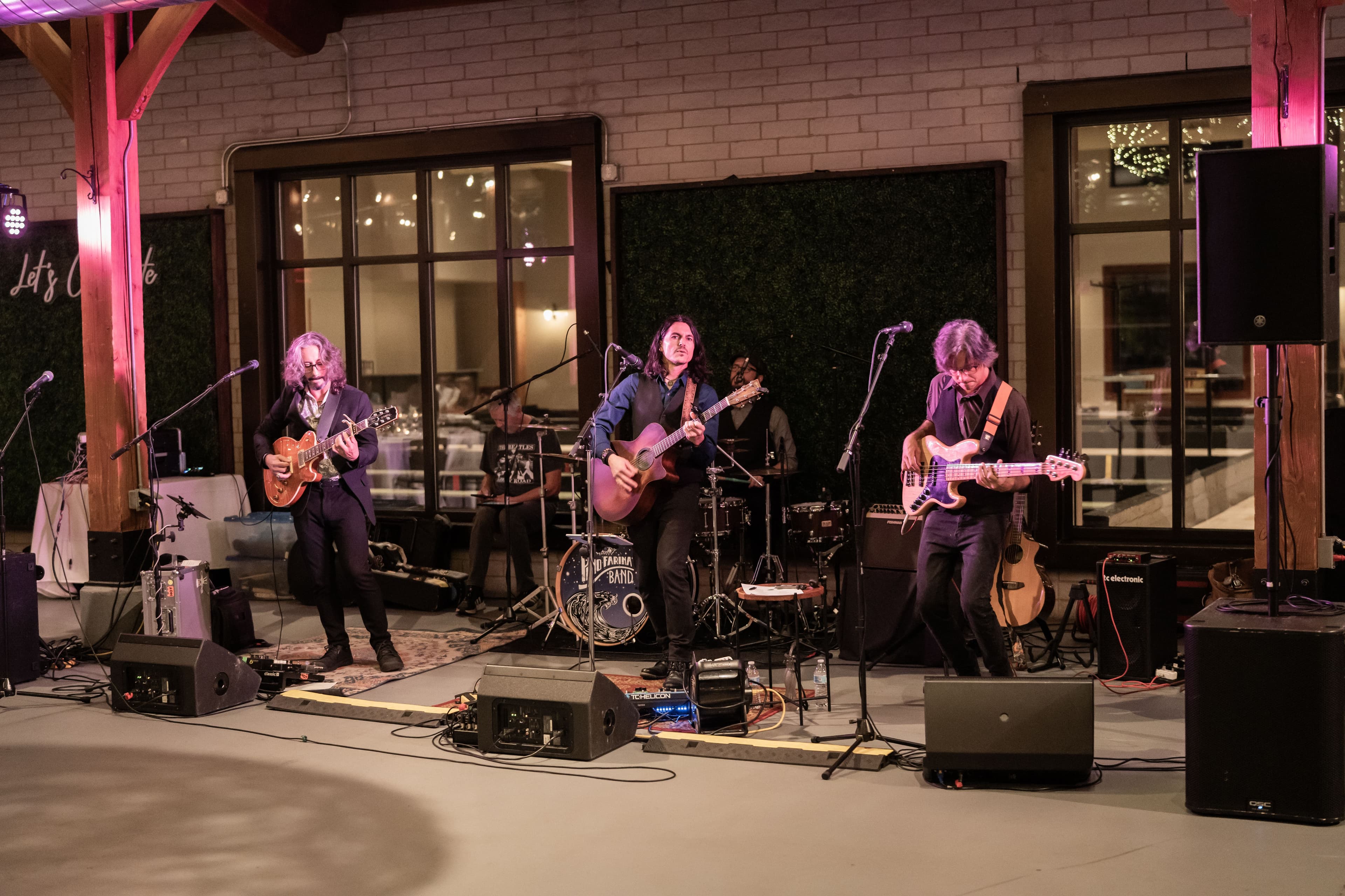 Band with drummer, guitarist, bassist, and lead vocalist with guitar performing on Pinstripes patio