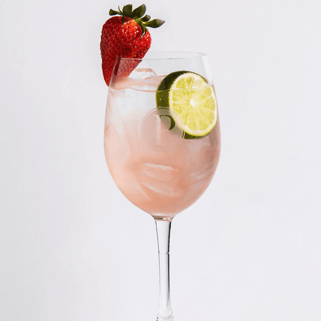 Light pink berry tequila spritz in a Pinstripes logo glass with strawberry and lime garnish from the summer spritz menu