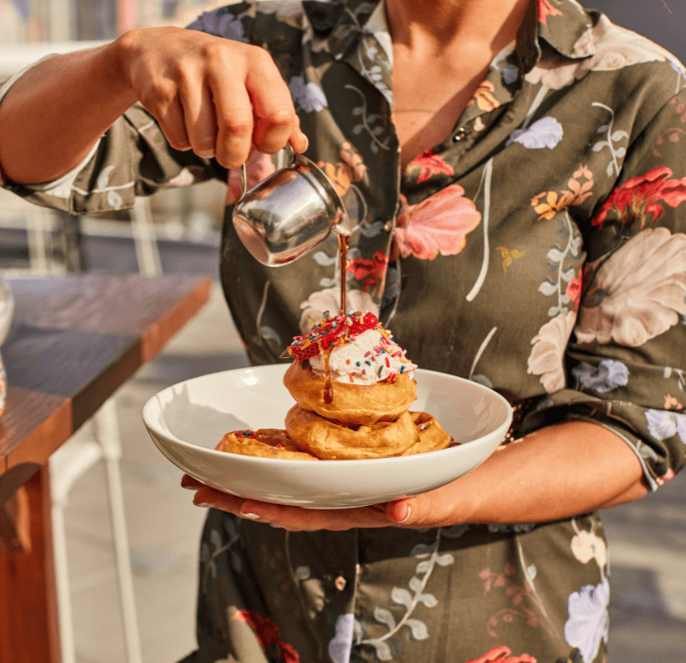 Woman holding plate of mini waffles from Pinstripes brunch buffet with toppings while drizzling syrup