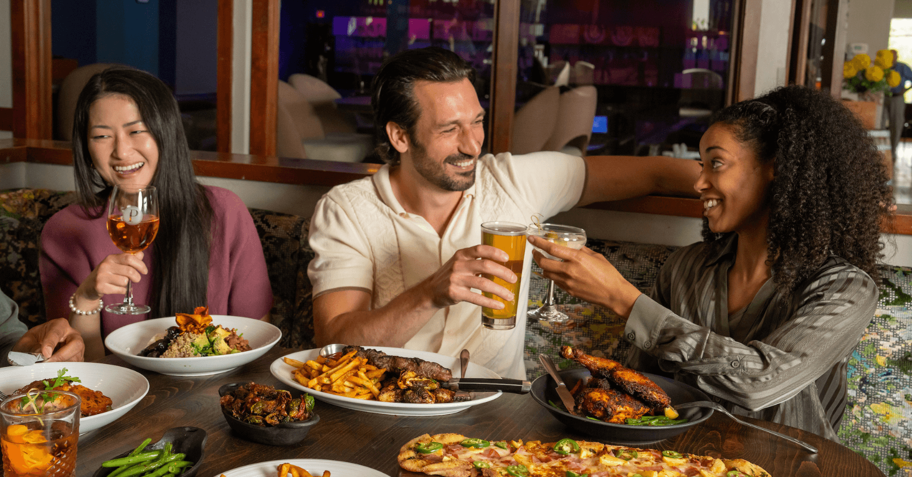 Three friends enjoying dinner with Super Salad, Rustic Chicken, Hawaiian Flatbread, Chimi Steak and shareable sides.