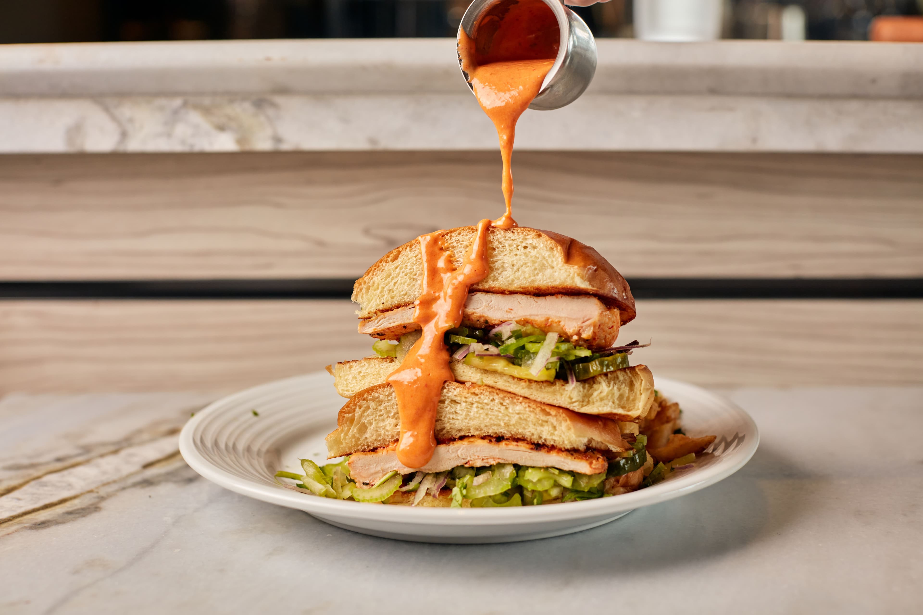 Spicy Crispy Chicken Sandwich from Pinstripes with sauce being poured over it.