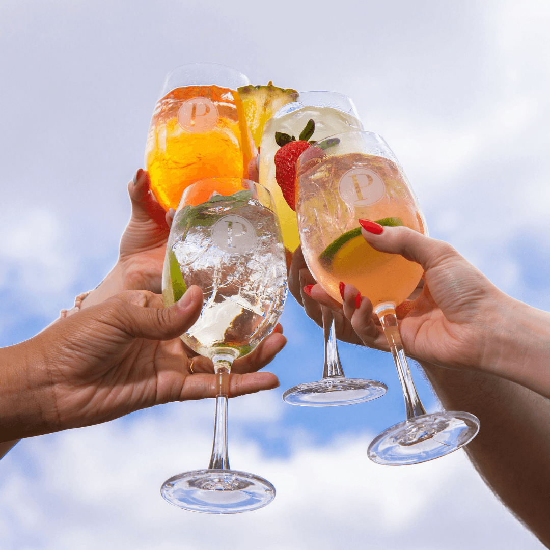 Guests clink glasses of Aperol, Hugo, Tropical, and Berry Summer Spritz cocktails in a cheerful toast.
