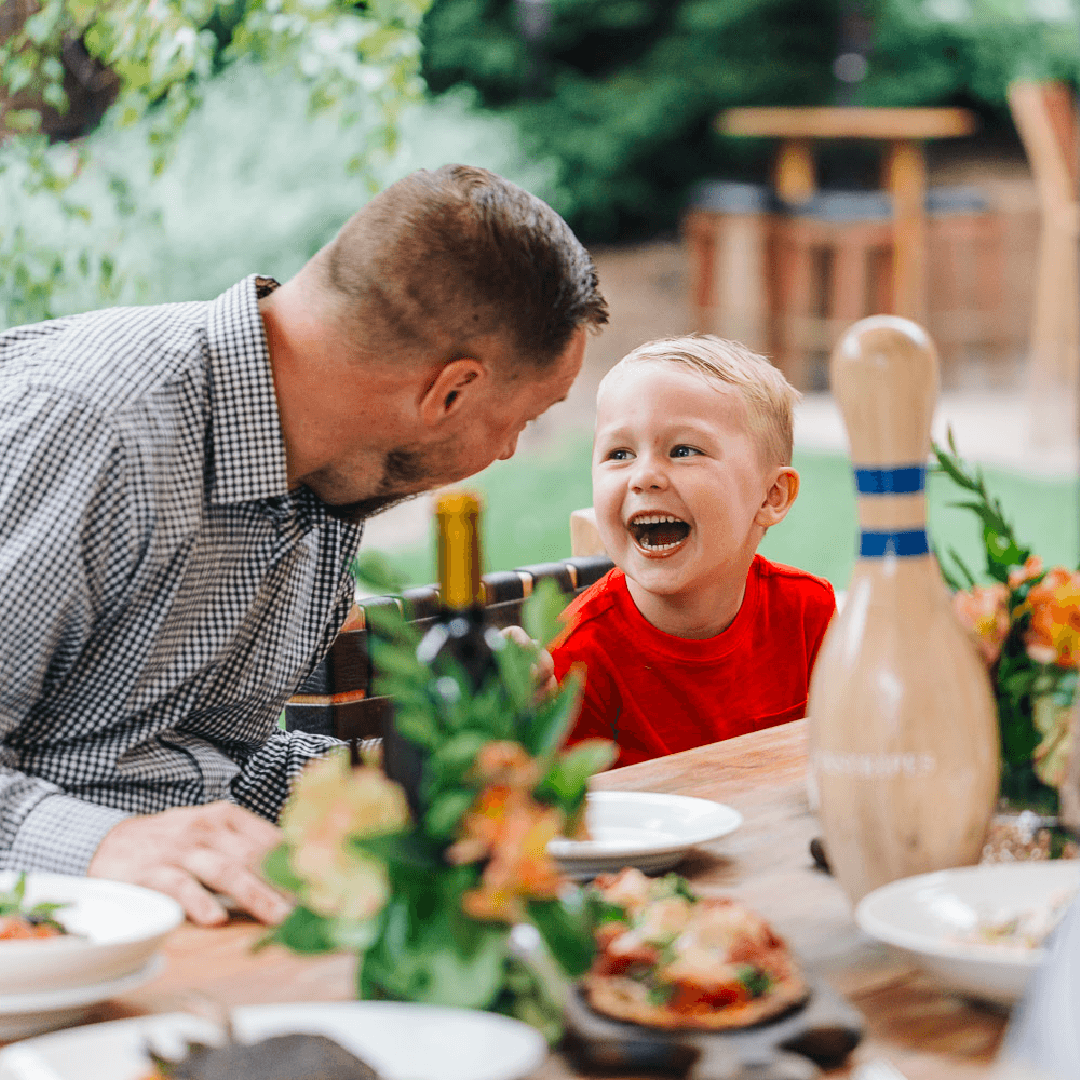 A dad and his son smiling at each other at the dinner table.