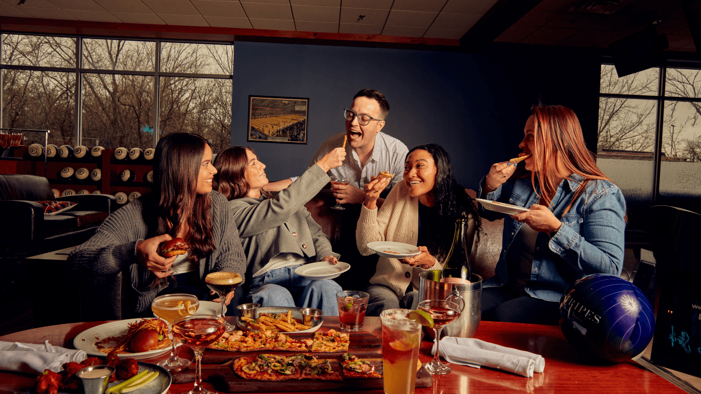 Group of friends bowling at Pinstripes while eating and drinking together