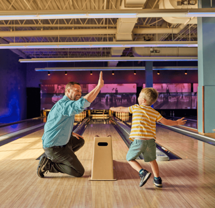 Father and son high-fiving on a bowling lane at Pinstripes