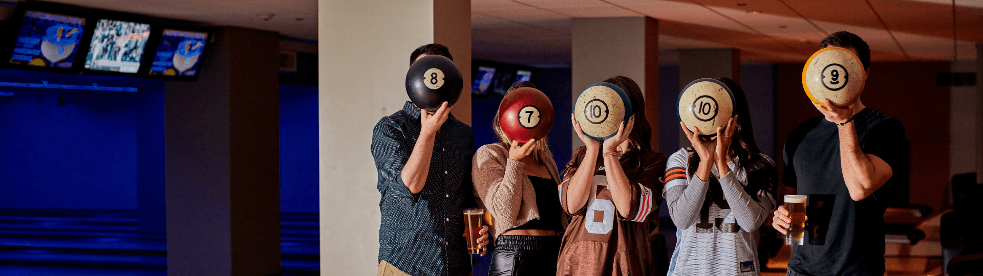 Five friends playfully holding colorful bowling balls in front of their faces.