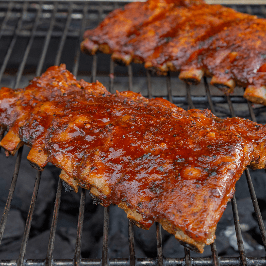 Two racks of ribs slathered with barbecue sauce on a grill.