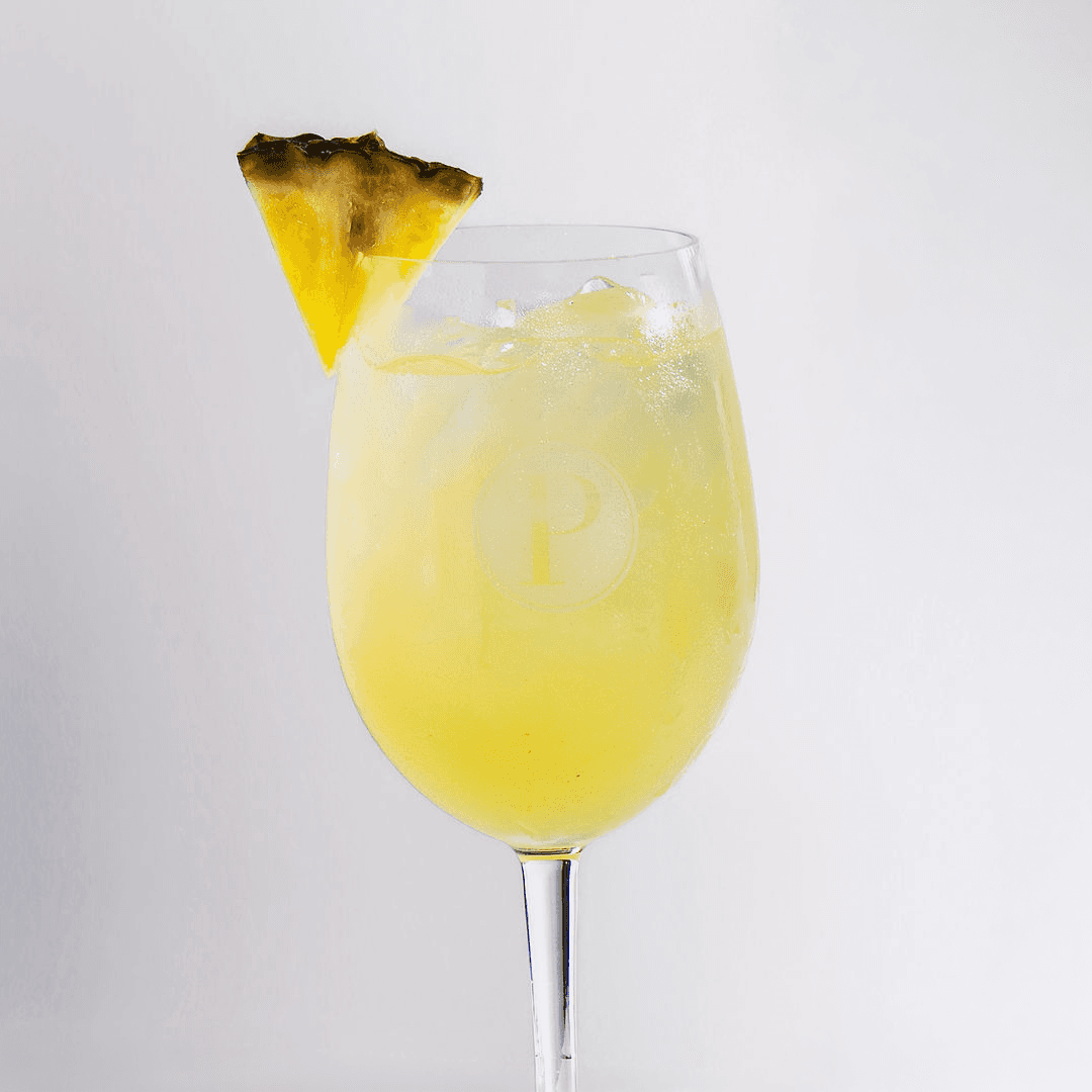 Tropical pineapple vodka spritz in a Pinstripes logo glass garnished with pineapple on the summer spritz menu
